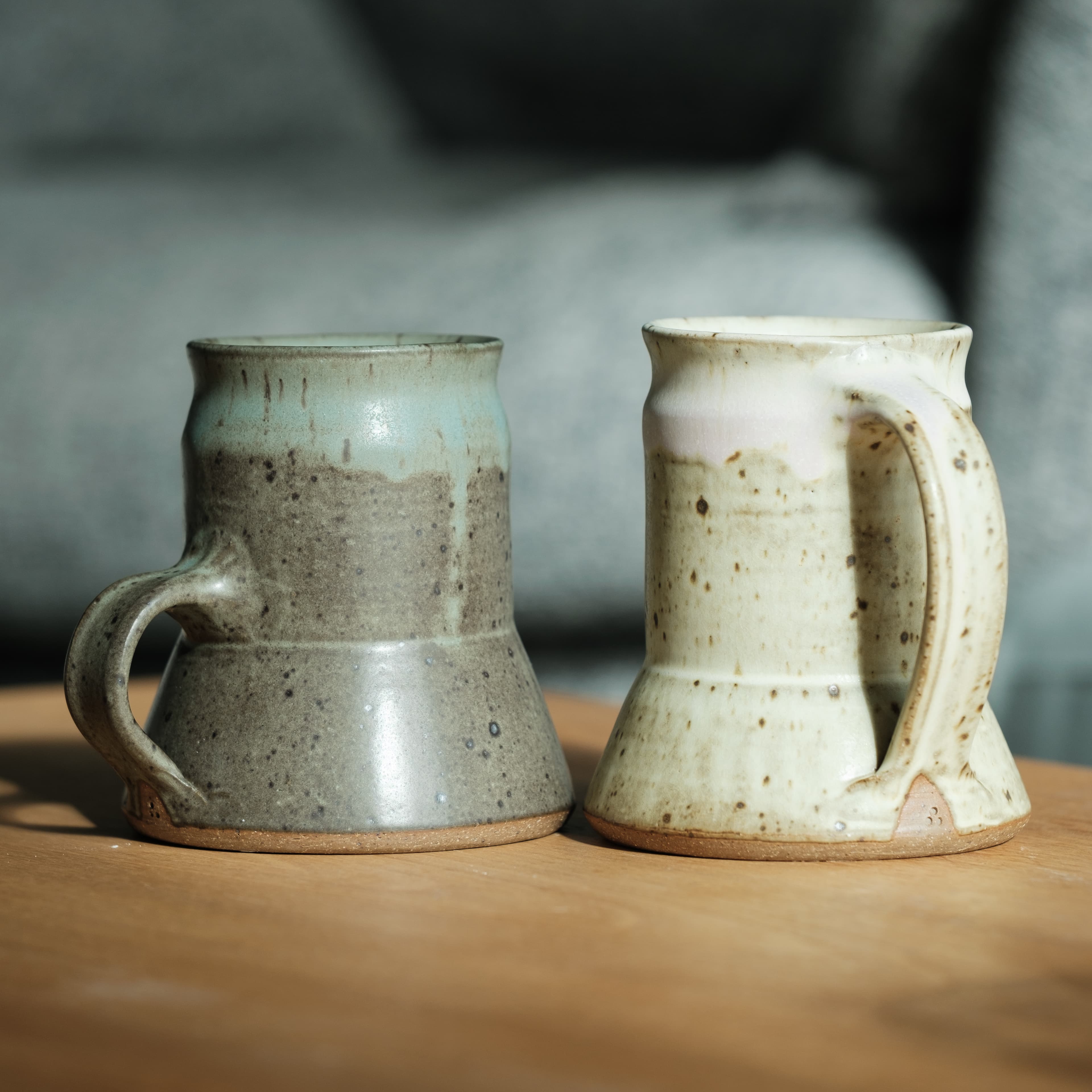 A pair of captain's mugs, one white, one green, sitting on a wooden surface.