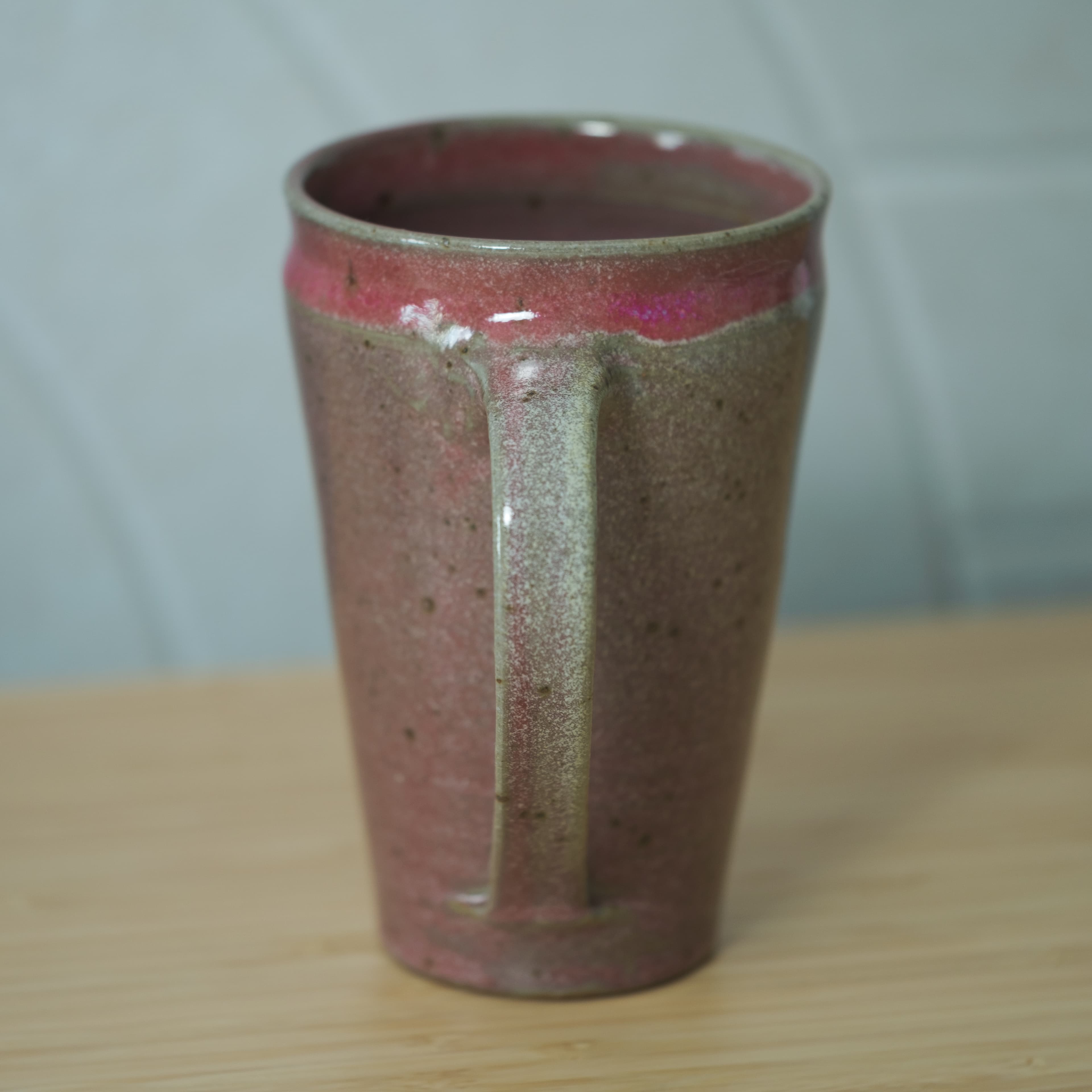 A delicately-handled, pink mug with a narrow foot. Its color fades to clear towards the bottom of the mug.