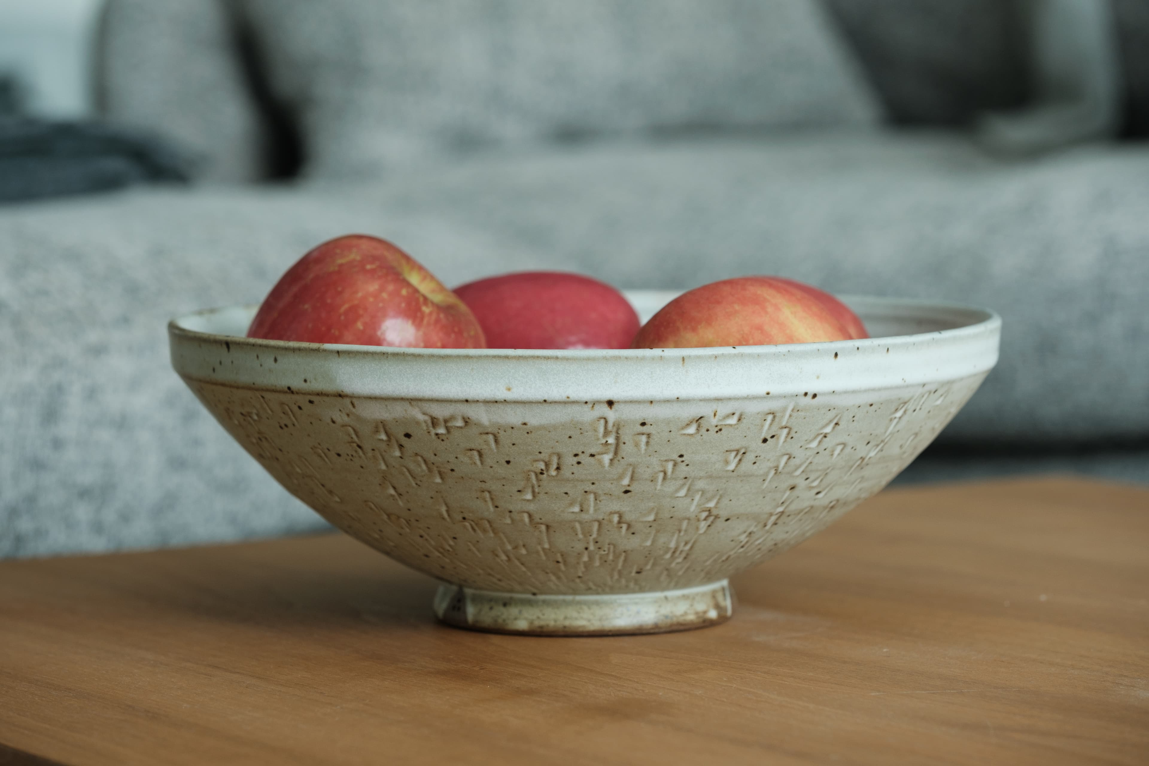 Wide, speckled white chattered bowl on a tall foot. It's got an angular rim, and is filled with red apples.